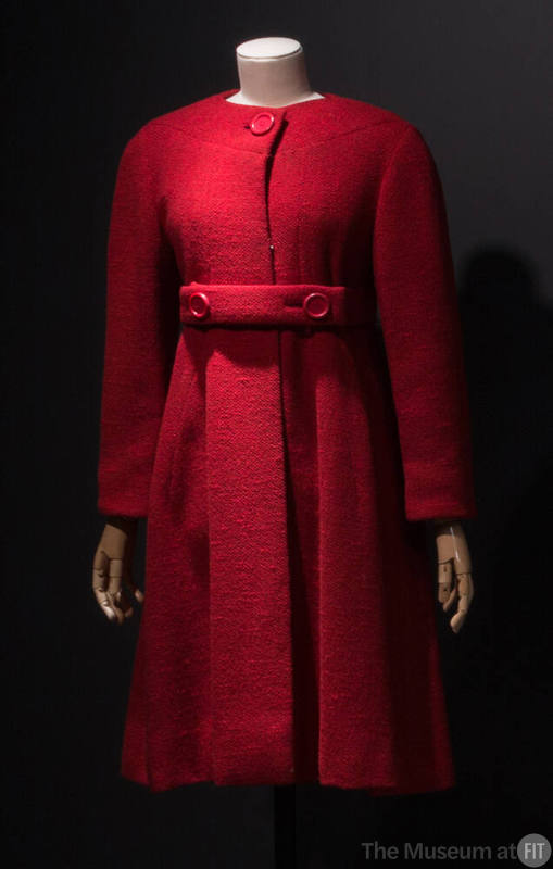Red collarless coat flared from waist with large red button neck closure and matching belt with…