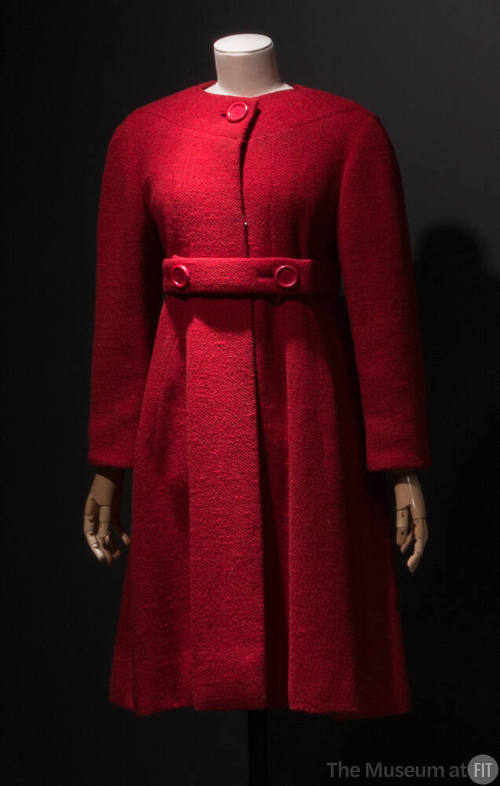 Red collarless coat flared from waist with large red button neck closure and matching belt with…