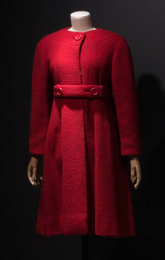 Red collarless coat flared from waist with large red button neck closure and matching belt with…