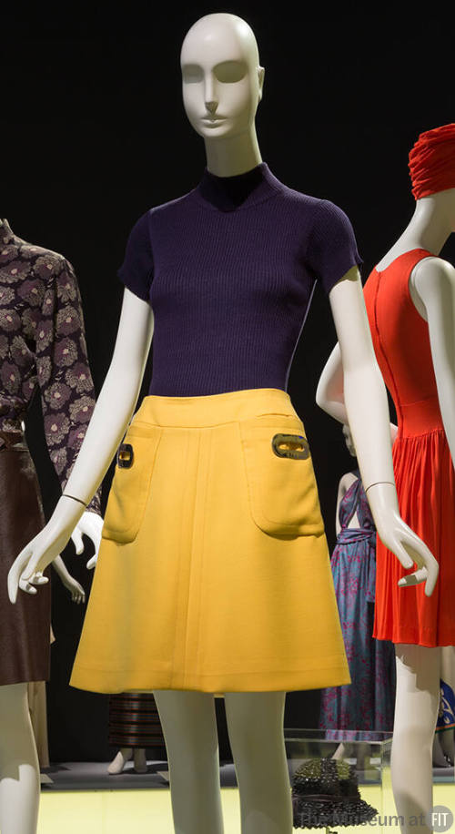 Navy blue short sleeved mock neck sweater and yellow mini skirt with large pockets at both hips