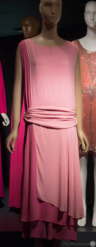 Pink tunic style sleeveless evening dress with attached dropped waist cummerbund, left side pan…