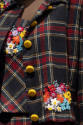 Detail of blue, red, green plaid jacket with yellow buttons and embroidered floral patch