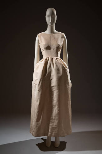 Sleeveless ivory dress with fitted bodice and long straightline skirt gathered at curved drop w…