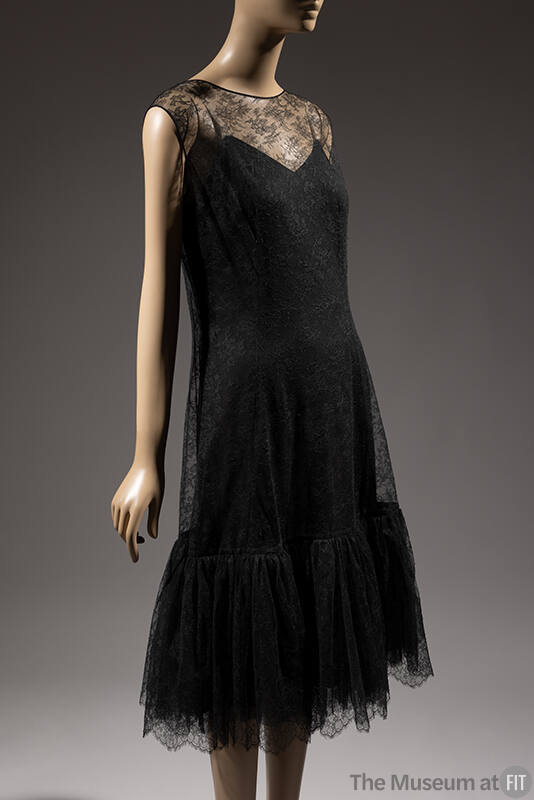 Sleeveless black net lace dress with round neck and scalloped hem ruffle over black slip