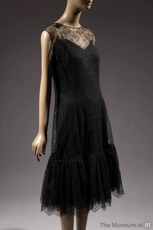 Sleeveless black net lace dress with round neck and scalloped hem ruffle over black slip