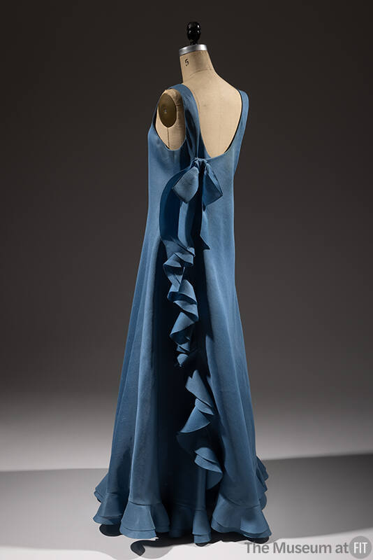 Back view of blue sleeveless dress with bow and row of ruffles down the side 