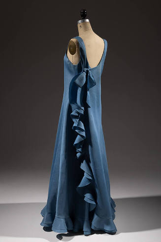 Back view of blue sleeveless dress with bow and row of ruffles down the side 