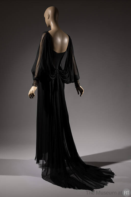 Back view of black silk floor length dress with sheer long dolman sleeves, skirt train 