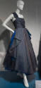 Grey one shoulder sleeveless evening dress with draping at waist revealing blue underskirt of a…