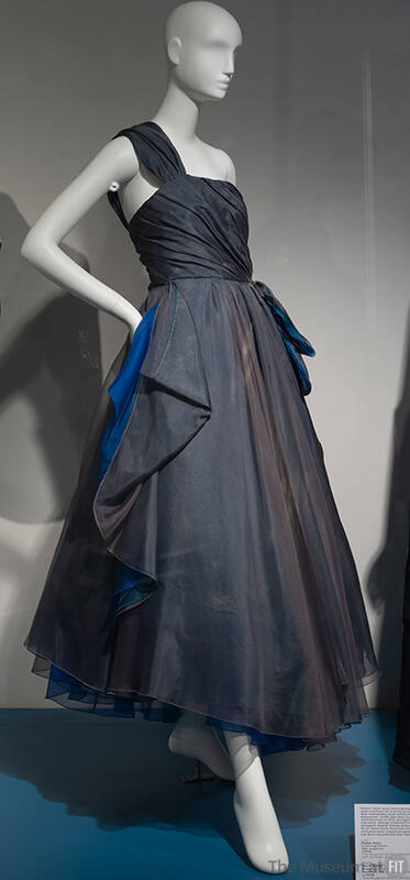Grey one shoulder sleeveless evening dress with draping at waist revealing blue underskirt of a…