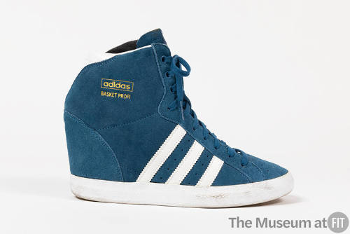 Blue sneaker with three white stripes on side and collar extending over the ankle with gold “Ad…