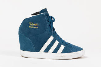 Blue sneaker with three white stripes on side and collar extending over the ankle with gold “Ad…