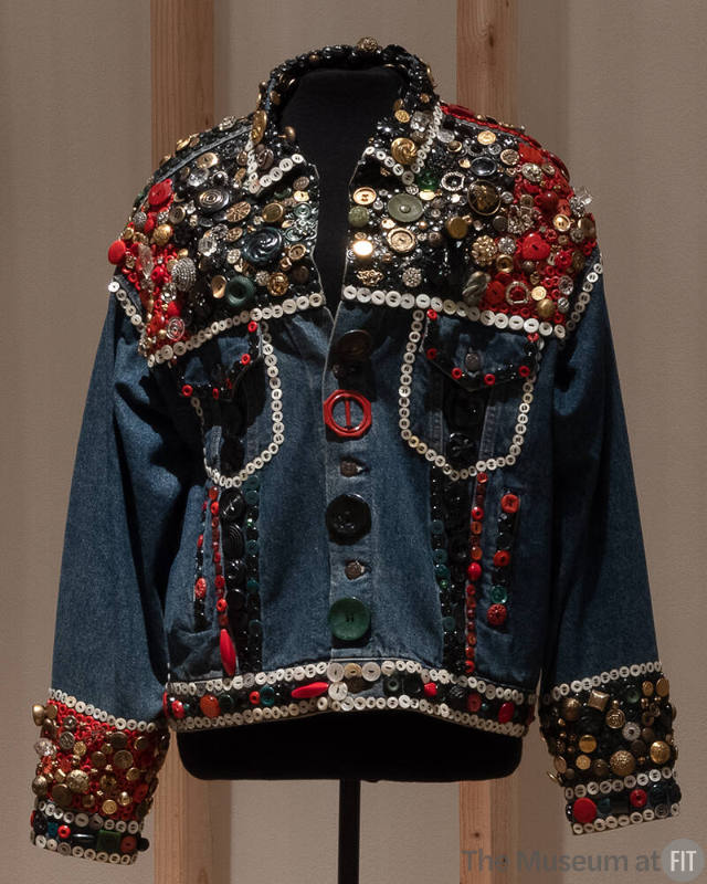 Blue denim long sleeve jacket covered with multicolor buttons at shoulders, cuffs and waistband…