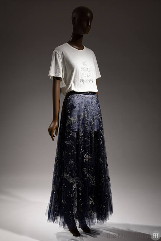 White t-shirt that reads We Should All Be Feminists, blue floor-length skirt with silver metall…