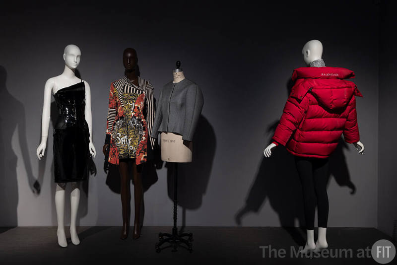 Dior + Balenciaga, Left to right: 2008.60.1 (black one shoulder dress), 2005.23.1 (graffiti knit dress), 2019.21.1 (jacket), 2016.113.1 (red puffer coat)