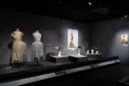 Designing Women exhibition installation view of two mannequins in dresses, five hats in cases, …