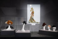 Designing Women exhibition installation view of five hats in cases and an image of a dress supe…