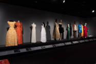 Designing Women exhibition installation view of eleven dressed mannequins on a dimly lit platfo…