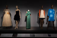 Designing Women exhibition installation view of five dressed mannequins on a dimly lit platform…