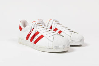 Pair of white sneakers with three red stripes on either side, white molded rubber toe cap and w…