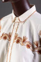 ¾ detail view of muslin poncho style top showing collar, button front and red and brown embroid…