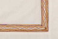 Detail view of red and brown embroidery corner on muslin poncho style top