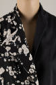 Detail view of black sleeveless collarless jacket with right half in off-white splatter print a…