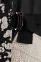 Detail view of black and off-white jacket showing half belt closure with silver buckle and text…