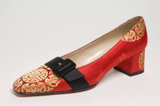 Red evening pump brocaded with red and gold Chinese inspired motifs, black belt across vamp and…