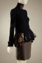 ¾ view of navy blue jacket showing long front panels of jacket draping over large brown ruffle …