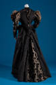 Back view of dark grey dinner dress showing cisele velvet extending from neck down center of dr…