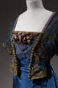 Detail view of mock bolero with gold thread embroidered design, short sleeve, and flowers on bl…