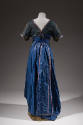 Back view of long blue gown, v neck back and floor length sash with purple trim