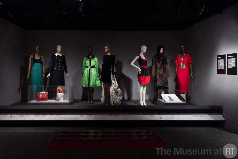 Platform featuring Twentieth century Latin American designers in the exhibition ¡Moda Hoy! Latin American and Latinx Fashion Design Today. From left to right: 78.147.3 (green gown), 93.129.10 (black dress), 98.102.5 (bag case), 77.190.28 (hat case), 2005.71.3 (green dress), 2005.48.8 (black dress), 2010.63.1 (black and red dress), 98.38.2 (coat), 2010.55.1 (red suit), 98.84.1 (sketch case)