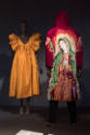 ¡Moda Hoy! exhibition installation view of two mannequins in a yellow dress and a red coat with…
