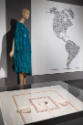 ¡Moda Hoy! exhibition installation view of a mannequin in a teal dress, a graphic of the Americ…