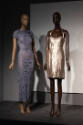 ¡Moda Hoy! exhibition installation view of two mannequins in a grey dress and a metallic gold d…