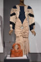 ¡Moda Hoy! exhibition installation view of a mannequin in a taupe dress with a brown bag in a c…