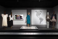 ¡Moda Hoy! exhibition installation view of five dressed mannequins, a wall screen, a graphic of…