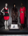 ¡Moda Hoy! installation view of three mannequins in a black and red dress, a dark brown fur coa…