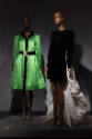 ¡Moda Hoy! installation view of two mannequins in a bright green dress and a black dress with a…