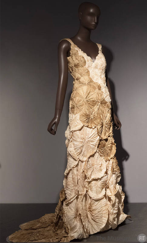 Sleeveless beige and off-white floor length dress covered with circular rosettes 