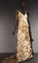 Sleeveless beige and off-white floor length dress covered with circular rosettes 