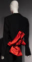 Back view of black jacket with slightly flared sleeves and large red/orange bow at waist