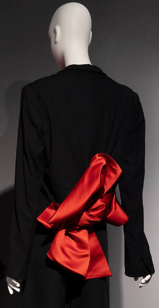 Back view of black jacket with slightly flared sleeves and large red/orange bow at waist