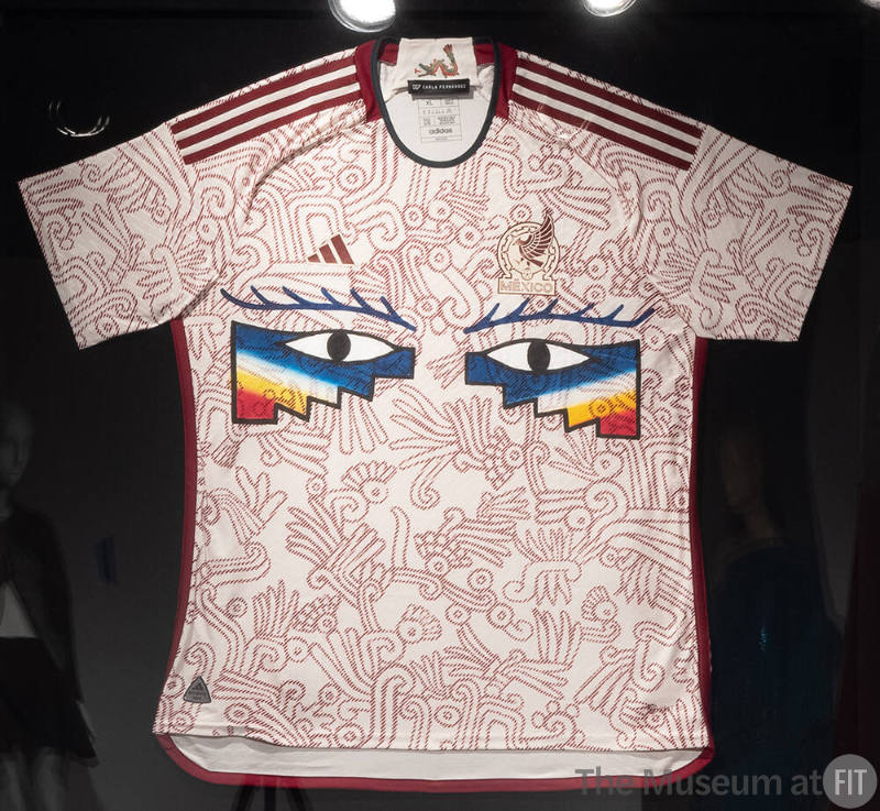 Off-white short sleeve athletic jersey with allover red print of Mixtec and Aztec deities and b…