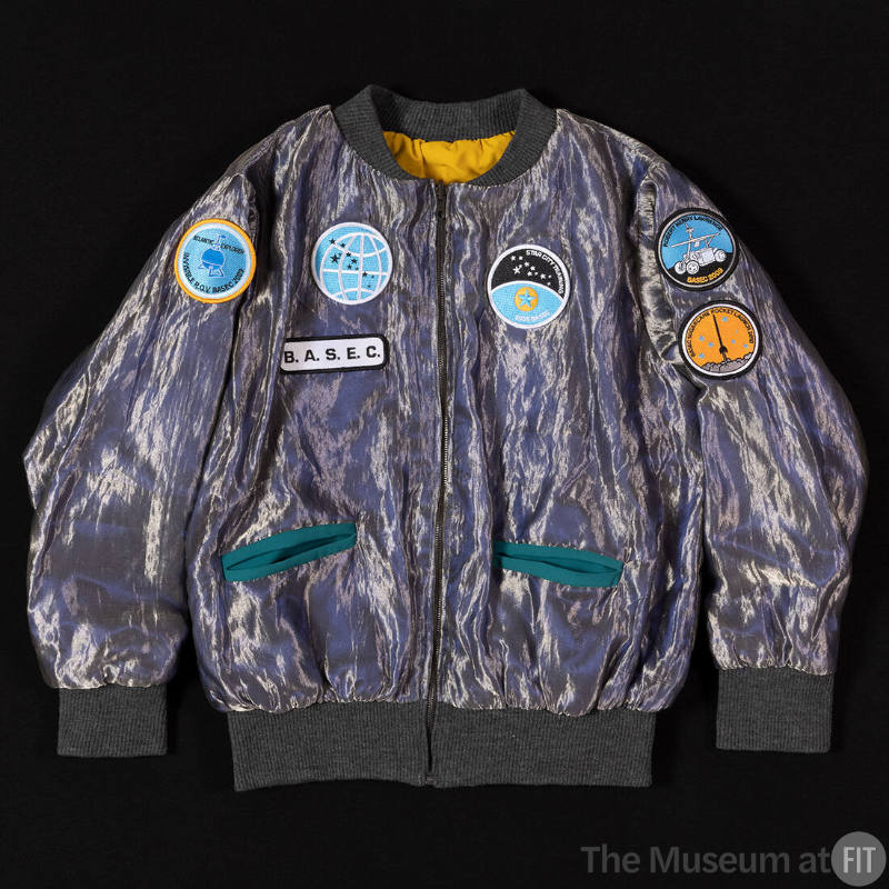 Silver metallic zip front jacket with two green slash pockets and multiple space patches