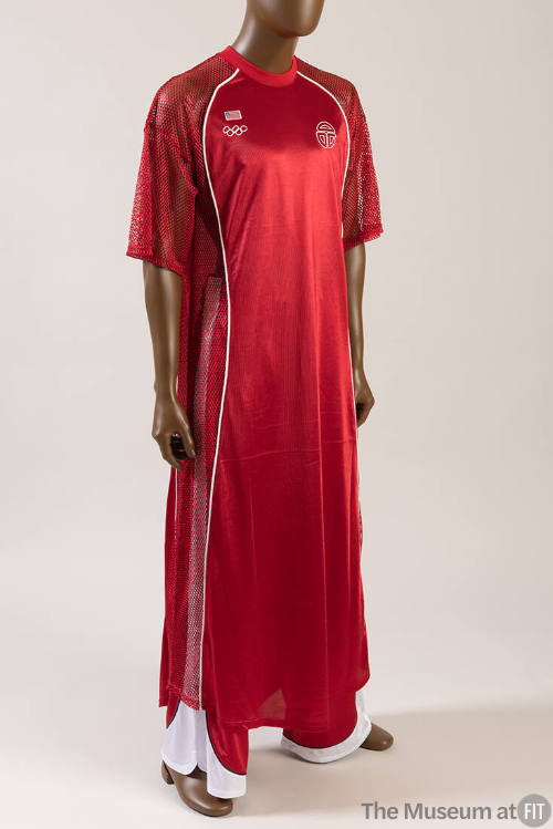 Red uniform jersey top, net sleeves and side panels, white Olympic rings logo on chest, red and…