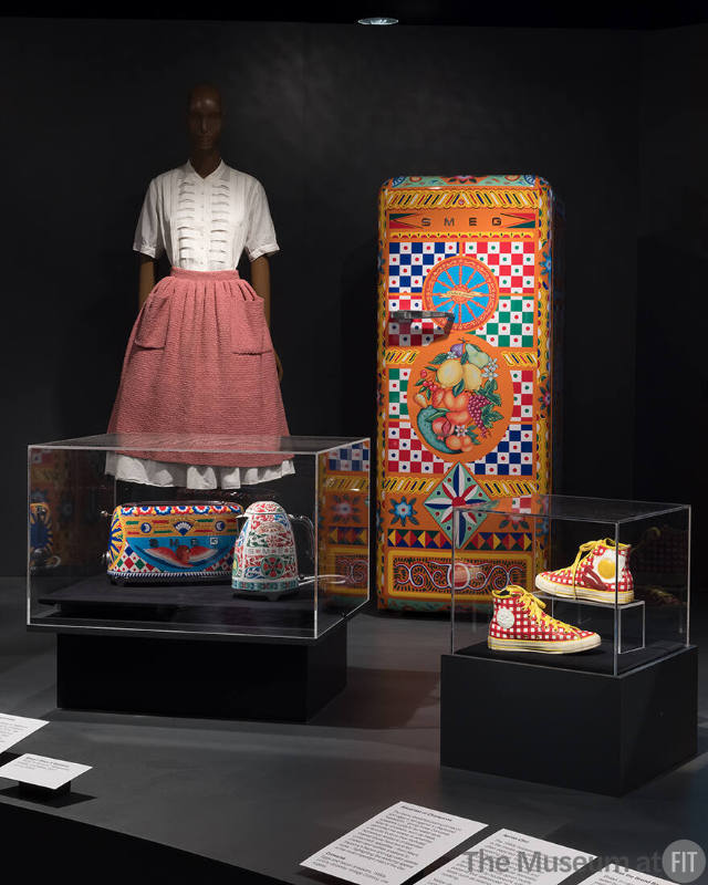 background) Bonnie Cashin, pink cotton and Lurex bouclé apron and matching necktie, 1949-1959. The Museum at FIT, Gift of The Estate of Bonnie Cashin; Smeg x Dolce & Gabbana, “Sicily is My Love” refrigerator, 2017. Lent by SMEG; (foreground) Smeg x Dolce & Gabbana, “Sicily is My Love” toaster and kettle, 2017. Lent by SMEG; Converse, eggs and bacon sneakers, 1980s. Lent by Golyester Vintage Clothing, Los Angeles