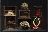 Food & Fashion exhibition installation view of a case containing produce themed hats, bags and …